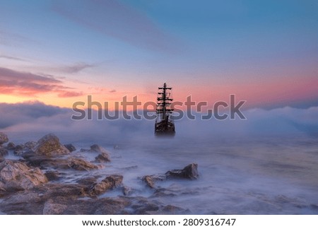 An old sailing ship in the mist sails towards the rocks - Sailing old ship in a storm sea in the background stormy clouds