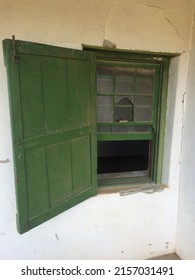 Old Sash Window With Broken Pane, And Shutter Painted Green, Set In A White Wall.