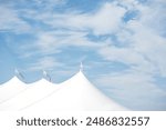 Old Saybrook, Connecticut USA, 7-11-2022   White Sperry Tent with Flags Blowing in the wind against a blue cloudy sky with a seagull overhead at an outdoor wedding