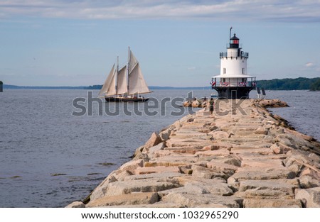 Old schooner sails past Spring Point lighthouse on a warm summer day in Portland Maine. Windjammers, as they are called, are a favorite tourist attraction in Maine.