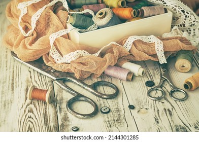 The old scissors, spools of thread, fabric and buttons on the wooden table, vintage concept.	