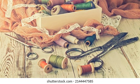 The old scissors, spools of thread, fabric and buttons on the wooden table, toned. Vintage concept.
