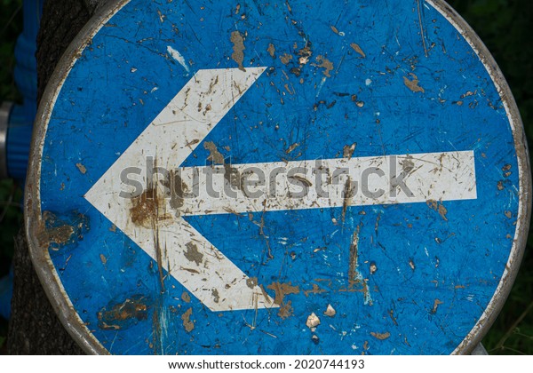 An old scratched blue street sign with an\
arrow in the middle showing to the\
left