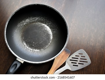 Old scratched non-stick pan on wood table. Teflon pan peeling off. Copy space is on the right side. 