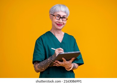 Old Senior Asian Female Grey Hair And Tattoo With Glasses Wear Hospital Uniform Standing With Confident And Cheerful Expression Studio Shot Yellow Background,senior Old Asia Woman Hand Hold Tablet