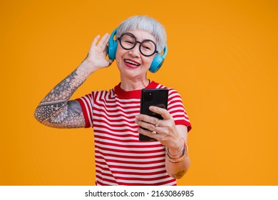 Old Senior Asian Female Listening Music Headphone And Smartphone  While Move Dance Positive Carefree Emotion Isolated On Yellow Background,asia Woman With Tattoo Happy Music Dance Sing Studio Shot