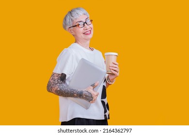 Old Senior Asian Female Woman Tattoo And Glasses Casual Cloth Business Owner Standing Hand Hold Laptop And Coffee Sup Confident Smile Isolate Yellow Background Studio Shot