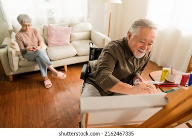 Old Senior Asian Male Using Art Therapy While His Legs Is Injured At Home,asian Elder Man Spend Recovering Of His Leg Is Getting Better With Painting Canvas Art In Living Room With His Wife At Home