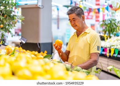 Old Senior Asian Man Looking At Tangerine While Enjoying Grocery Shopping At In The Supermarket