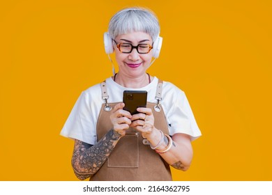 Old Senior Asian Woman Wear Apron Hand Choosing Music Playlist From Smartphone Relax Casual Lifestyle,asia Tattoo Woman Wear Headphone Listen Music Carefree Isolate Yellow Background Studio Shot