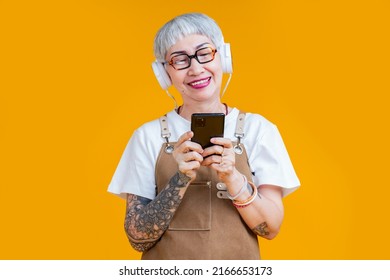 Old Senior Asian Woman Wear Apron Hand Choosing Music Playlist From Smartphone Relax Casual Lifestyle,asia Tattoo Woman Wear Headphone Listen Music Carefree Isolate Yellow Background Studio Shot