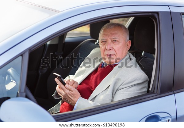 Old Senior business man driving a car and texting\
on a mobile phone