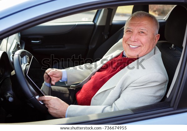 Old senior business man\
with tablet pc computer on driver seat looking to camera and smile\
with white teeth. Transport, business trip, technology and people\
concept