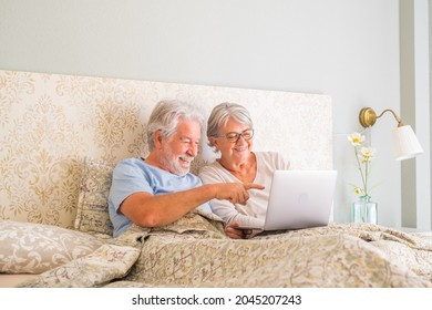 Old senior caucasian couple smiling and using laptop in the morning at bed in the bedroom at home. Elderly couple surfing and using social media on laptop at home. man pointing towards laptop screen - Powered by Shutterstock