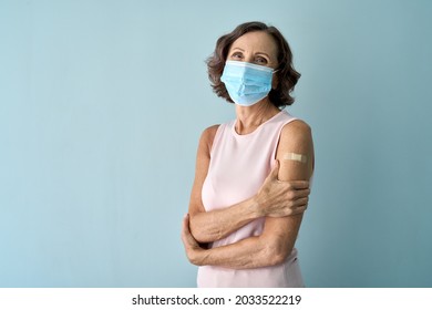 Old senior cheerful happy lady standing wearing face mask with plaster on shoulder after covid 19 vaccine isolated on blue background. Coronavirus vaccination campaign concept. Copy space. Portrait. - Powered by Shutterstock