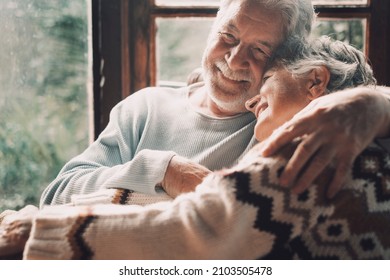 Old Senior Couple In Love Hug And Embrace With Romance Together At Home With Outside View In Windows Background - Happy Mature Retired People Lifestyle Enjoying Caring Each Other And Smiling
