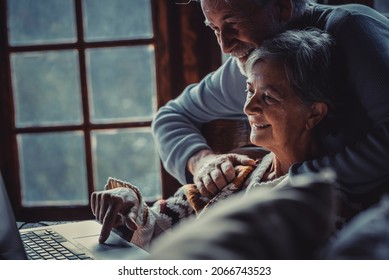 Old senior couple use laptop computer at home by night togethe smiling and enjoying internet online connection. Happy retired people man and woman surf the web and have fun with internet network - Powered by Shutterstock