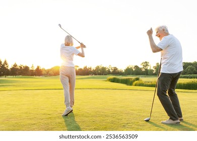 old senior couple in white clothes playing golf on golf course and chatting at sunset, elderly man and woman actively relaxing outdoors and laughing, pensioners on vacation - Powered by Shutterstock