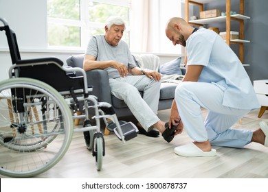 Old Senior Home Care. Nurse Helping Patient To Dress Shoes