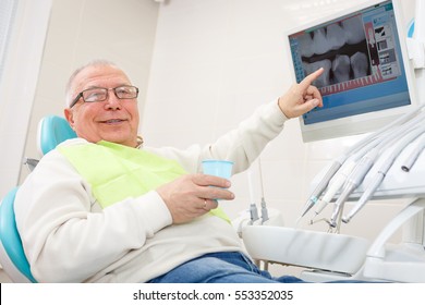 Old Senior Man In Dental Clinic. Sitting In A Chair And Look X-Ray On Computer