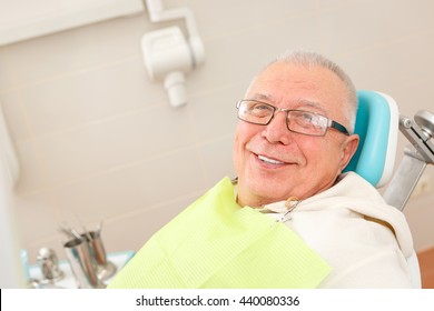 Old Senior Man With Glasses Sitting In A Dental Chair In A Dentist's Office.