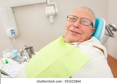 Old Senior Man With Glasses Sitting In A Dental Chair In A Dentist's Office.