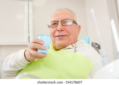 Old Senior Man With Glasses Sitting In A Dental Chair In A Dentist's Office.