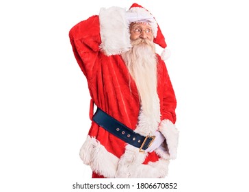 Old Senior Man With Grey Hair And Long Beard Wearing Traditional Santa Claus Costume Very Happy And Smiling Looking Far Away With Hand Over Head. Searching Concept. 