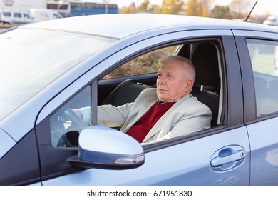 Old Senior Man Sitting In Car On Driver Seat And Keeps The Steering Wheel. Spring And Summer Time