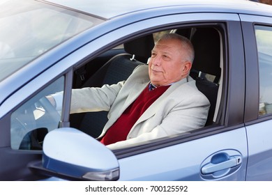 Old Senior Man Sitting In Car On Driver Seat And Keeps The Steering Wheel. Spring And Summer Time