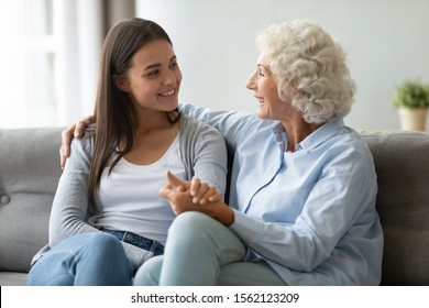 Old Senior Mother And Young Adult Daughter Talking Bonding Sit On Sofa, Smiling Elder Grandma Embracing Grown Granddaughter Having Trust Conversation, Two Age Generation Women Family Chatting At Home