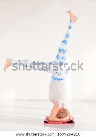 Old senior woman doing advanced yoga or pilates. Supported headstand, salamba sirsasana