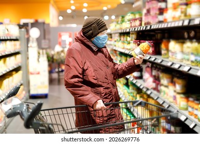 Old senior woman wear medical mask, protection against pandemic coronavirus disease. 90 years retired female lady push cart trolley for shopping in supermarket. Woman buy food and groceries