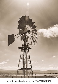 Old Sepia Photo Of A Windmill On A Farm. Image Is Shot Into The Sun