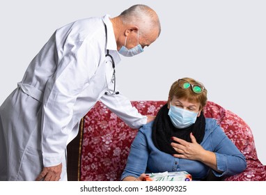 A Old Serious Doctor Wearing A Mask Checks The Well-being Of An Older Woman During A Medical Examination At Home. Virus And Pandemic Concept