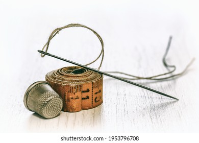 Old sewing accessories for sewing handmade on a white background, a tailor's tape, a needle and thread, a thimble. Needlework set. 