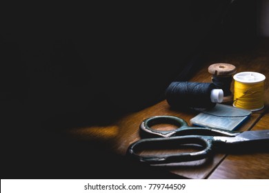 Old Sewing Machine With Black Thread Scissors And Needle, On A Old Grungy Work Table. Tailor's Work Table. Textile Or Fine Cloth Making. Industrial Fabric