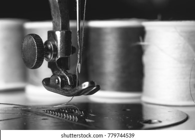 Old sewing machine with colour thread and needle, on a old grungy work table. Tailor's work table. textile or fine cloth making. industrial fabric black and white