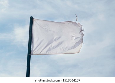 Old old, shabby, full of holes, dirty white flag waving with the wind against sky clouds.