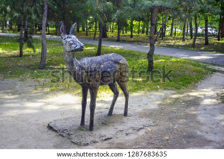 Old shabby sculpture of roe deer in a city park.