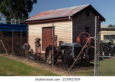 An Old Shed Surrounded By Old Farm Equipment In A Park On A Sunny Day