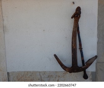 Old Ship Anchor Leaning Against A White Wall