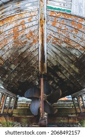 An old ship laid on the keel. Old and weathered wooden planks, the propeller can be seen. 