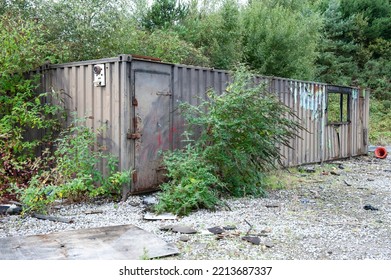 Old Shipping Container Office Unit. Damaged And Burned. Beyond Repair. Decaying Metal Structure With Windows And Plants Growing.