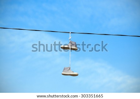 Old shoes hanging on an electric cable against blue sky.