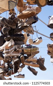 Old shoes hanging on a hills hoist washing line with light blue sky background.