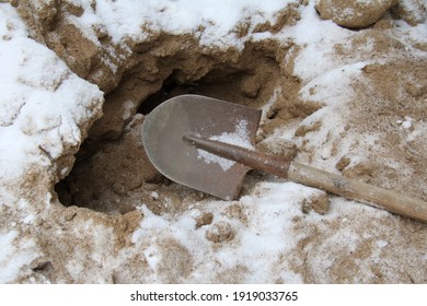 An Old Shovel In The Sand, Covered With Snow For The Groundbreaking Ceremony. The Concept Of Winter Chores, Sand For Sprinkling Snow Paths, Safety In The City In Winter.