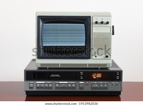 Old silver vintage TV\
with noise and interference on the screen and VCR on the background\
of the wallpaper.