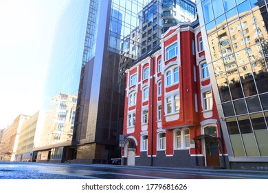 Old Small Red Brick Building Stands Between Two New Glass Buildings. There Are No Peopleon The Street. Theme Of Old And New.