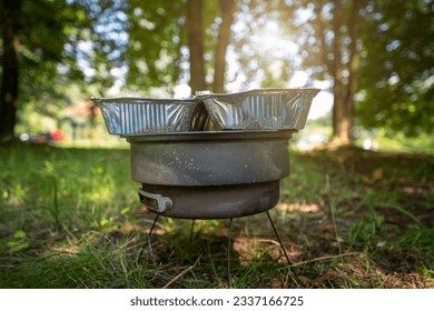 Old small rusty grill spread out on the grass in the park. The perfect outdoor grill. On the grill, 2 aluminum trays with food inside